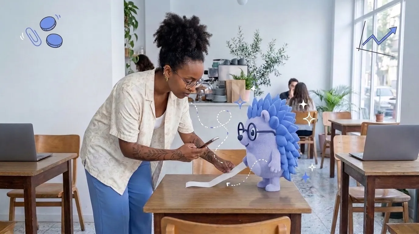 Noa, a graphic designer, works on her laptop in a café. Keepy, the Keep mascot, holds a receipt flat while she photographs it.